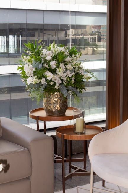A floral arrangement featuring a lush bouquet of predominantly white flowers, including roses and lisianthus, with accents of green foliage such as ferns and eucalyptus, displayed in a decorative gold