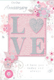 This anniversary card is displayed as though waiting beside a freshly delivered bouquet in a Morden home, its design quietly celebrating the beauty of lasting love. The central feature is the word "LOVE," written in large, raised letters that are dusted with soft blush-pink glitter. Each letter is rounded and slightly embossed, edged with a slim line of shimmering silver that catches the light with a gentle sparkle. The textured finish suggests a pleasant, lightly rough feel under the fingertips, inviting a slow, affectionate touch. Behind this, a smooth panel of pastel pink creates a calm and romantic backdrop, reminiscent of the delicate evening colours that sometimes wash over Morden Park. Encircling the central word, a pattern of stylised flowers and leaves drifts outward in airy spirals. These floral motifs are drawn in fine lines of pearly white and subtle grey, with occasional touches of silver that glint like tiny points of light among the petals. The blossoms suggest small, graceful garden flowers arranged in loose sprays, similar to the stems a local florist might combine in an anniversary bouquet-soft blooms interwoven with slender greenery. The swirling vines and filigree curls add a sense of movement, giving the impression that the flowers are gently leaning towards the word "LOVE," as foliage leans around focal roses in an arrangement. The lighting is soft and even, ensuring no harsh shadow distracts from the delicate textures and shimmer. Inside, part of an elegant script message about enduring affection and shared memories is visible, its curving lines echoing the motion of the illustrated vines. The card feels tender and thoughtfully designed, an ideal companion to anniversary flowers delivered throughout Morden, from homes near the station to quiet streets close to Morden Hall Park.